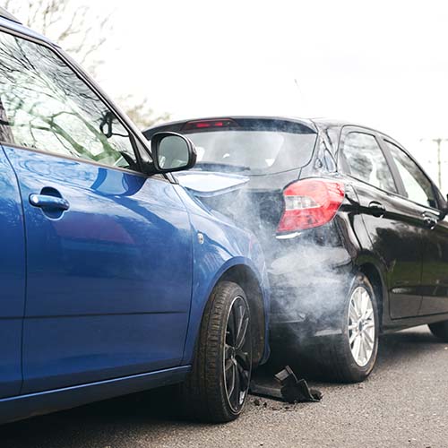 Two cars involved in a collision with smoke and damage on the road.
